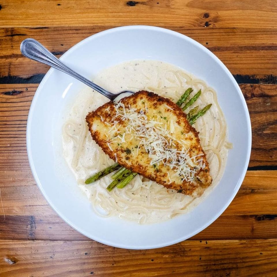 Breaded chicken parmesan with creamy pasta, asparagus, and a spoon in a white bowl.
