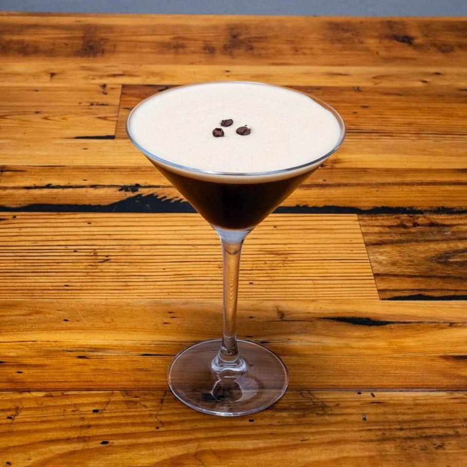 Espresso martini with creamy foam and three coffee beans on a rustic wooden table.