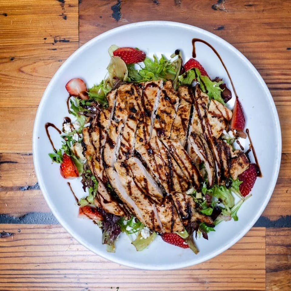 Grilled chicken salad with strawberries, feta, and balsamic glaze on a white plate.